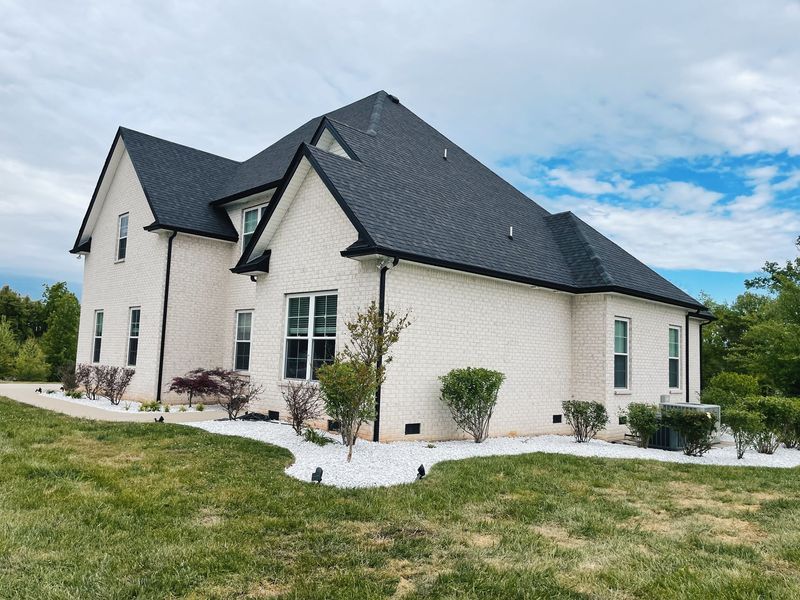 Two-story brick house with black roof, white trim, and small garden.