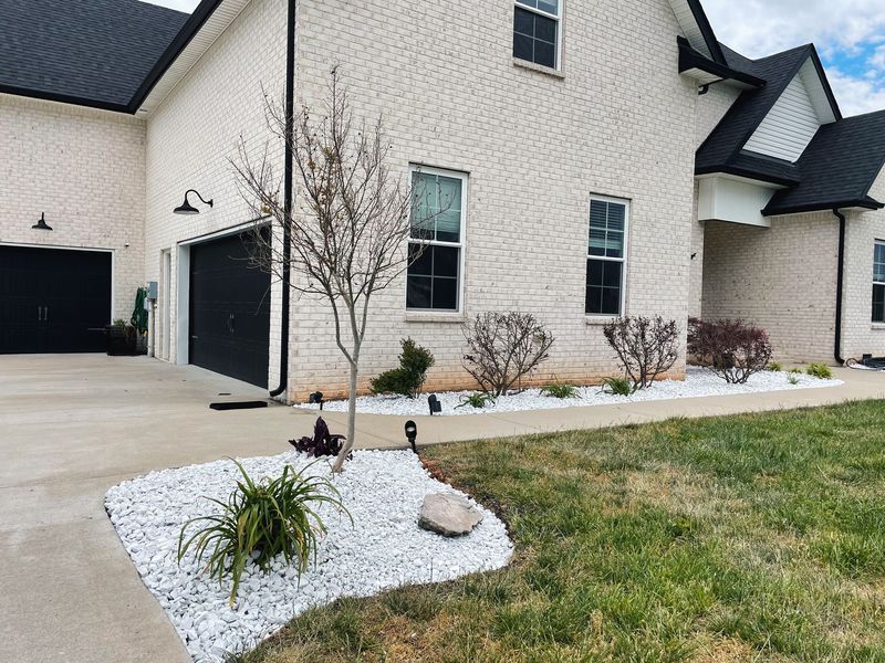 House exterior with white brick, black garage door, and rock landscaping.