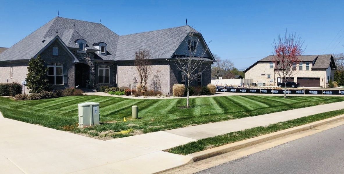 Large brick house with striped green lawn, blue sky.