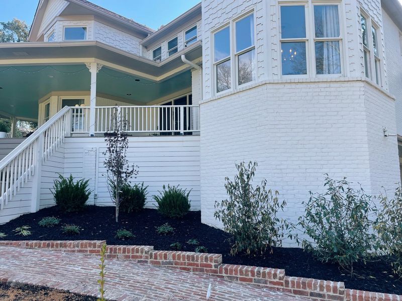 White house with porch and brick walkway, landscaping with dark mulch.