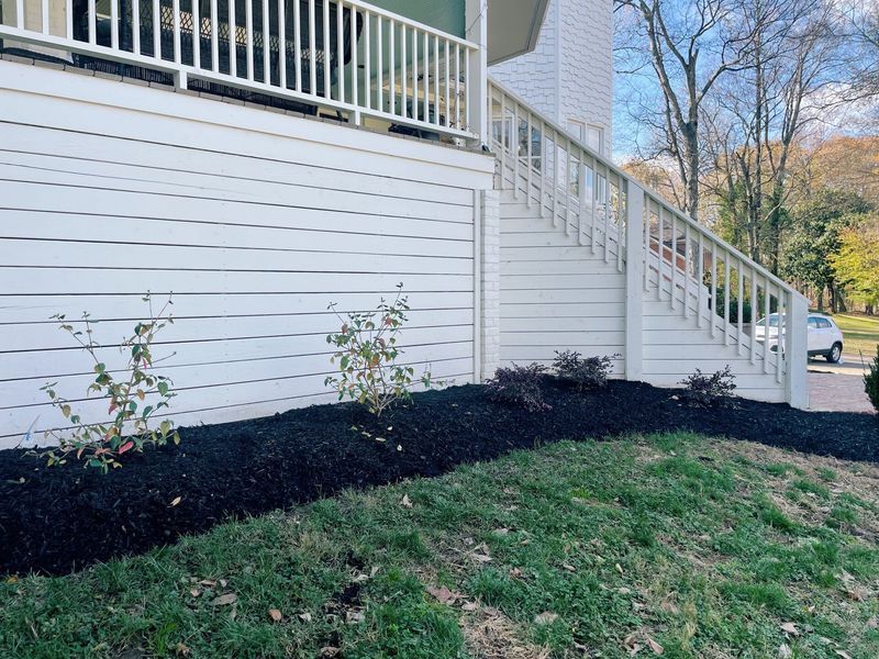 White house with stairs and a small garden with black mulch.