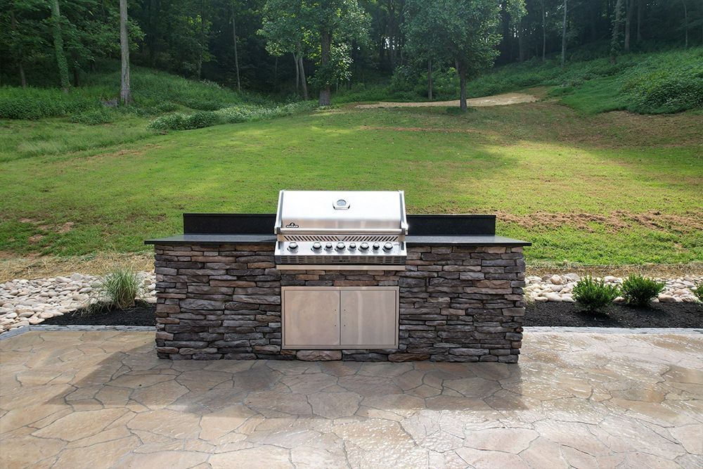 Outdoor grilling station with stone facade, stainless steel grill, and grassy background.
