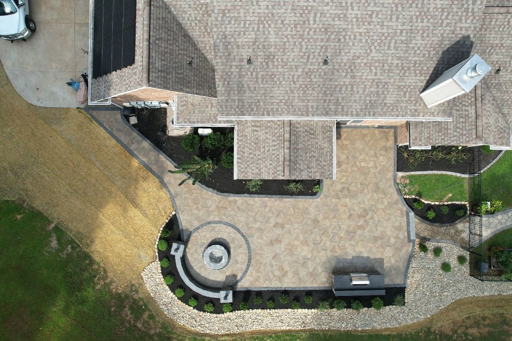 Overhead view of a house with patio, stone features, landscaping and a curved fire pit.