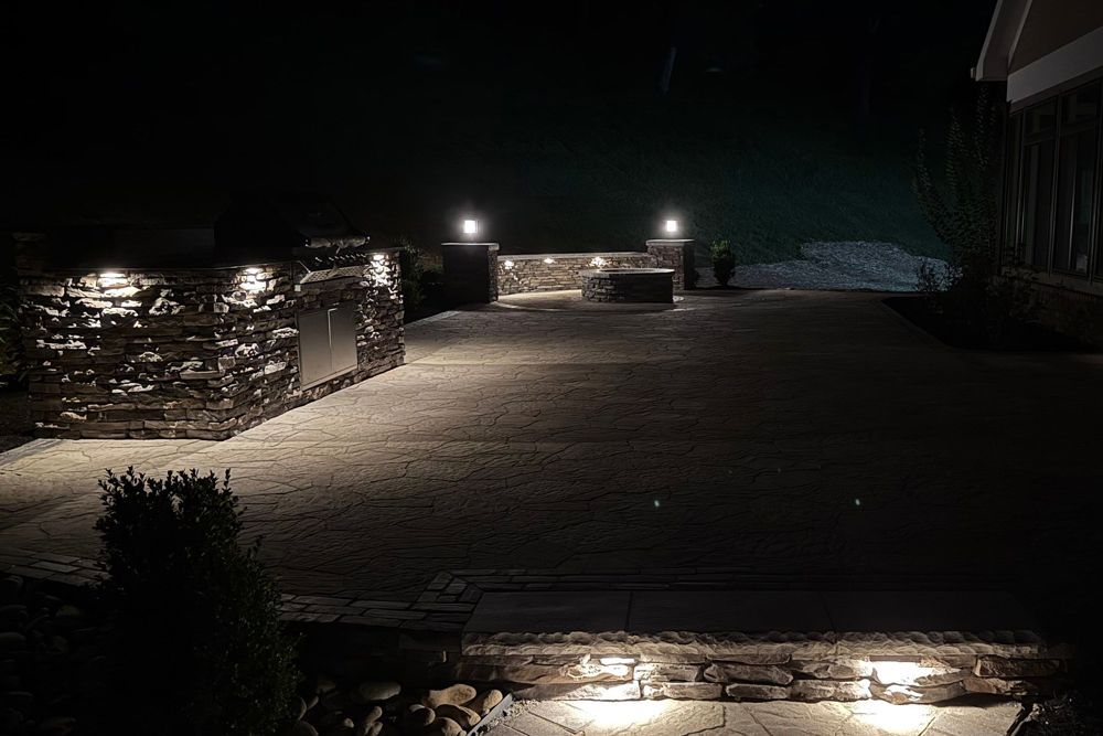 Nighttime view of a stone patio with lights illuminating the space. Dark sky and building visible.