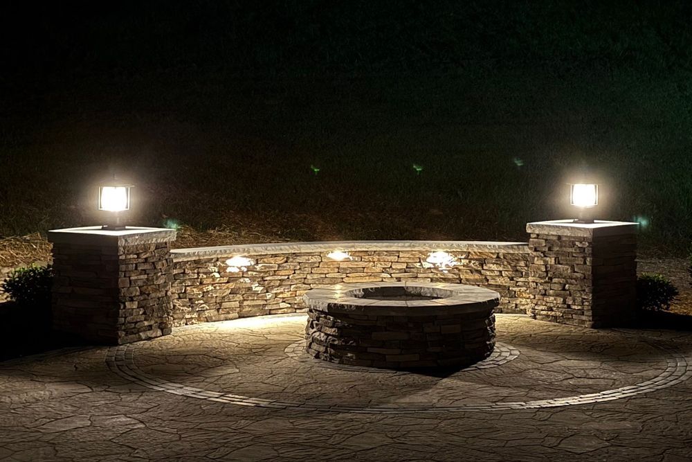 Stone fire pit and seating area lit at night.