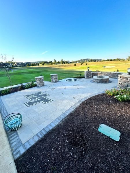 Patio with stone pavers and fire pits, overlooking a golf course on a sunny day.