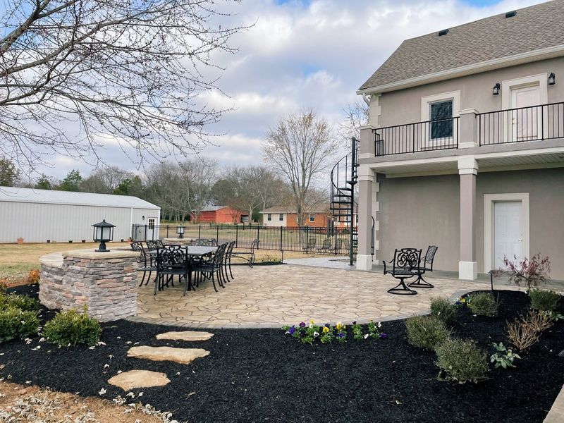 Backyard patio with dining set, spiral staircase, and manicured landscaping.