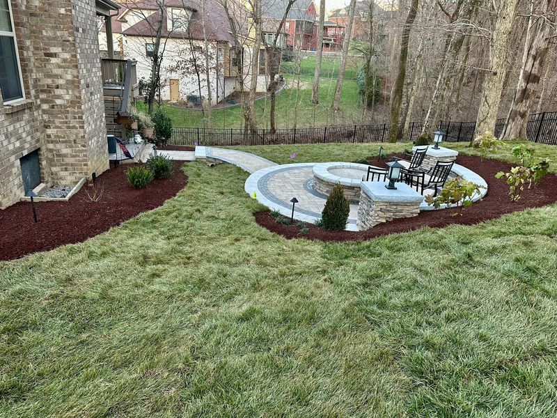 A landscaped backyard with a circular fire pit area, stone walkway, and manicured lawn.