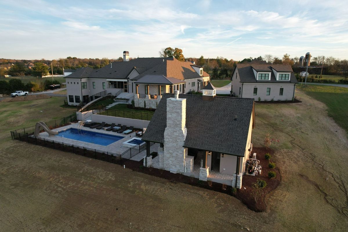 An aerial view of a large, luxury home with a pool and a detached building on a grassy lot.