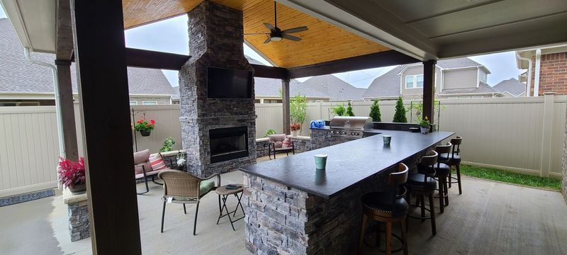 Covered outdoor patio with fireplace, bar, seating, and a ceiling fan.