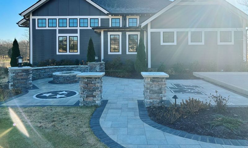 Gray house with stone patio, pillars, and landscaping. Pathway leads to entrance.