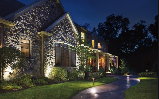 A stone house illuminated at night, pathway lit by lights.