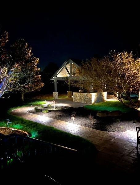 Night-lit outdoor patio with a gazebo, pathways, and trees. Pathway lights and gazebo lights provide illumination.