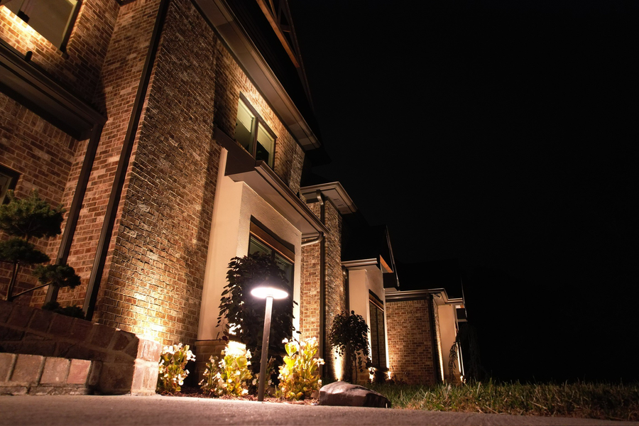 Nighttime shot of a brick building with illuminated landscaping and entryway; dark sky.