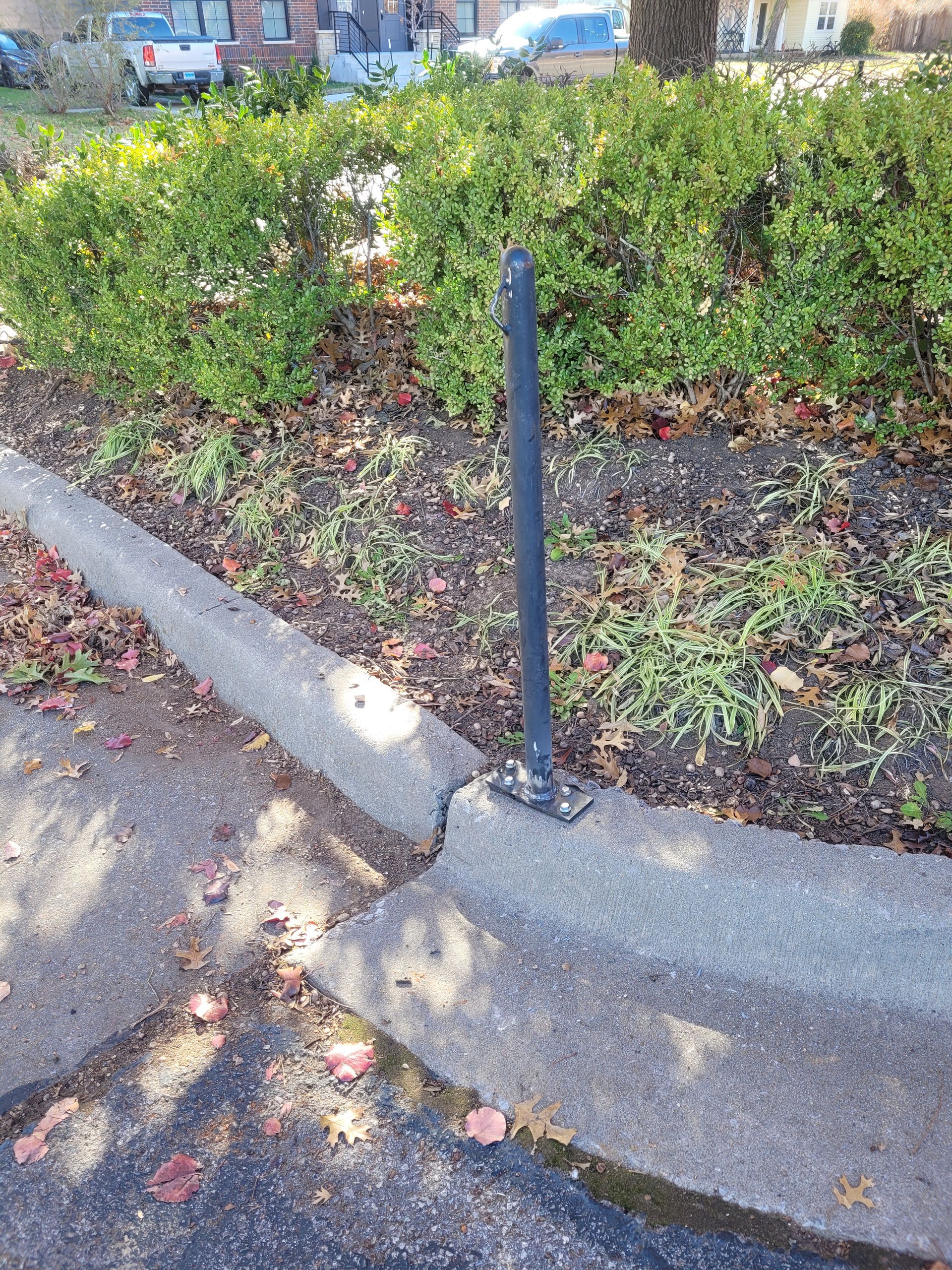 A black pole is sitting on the side of the road next to a curb.