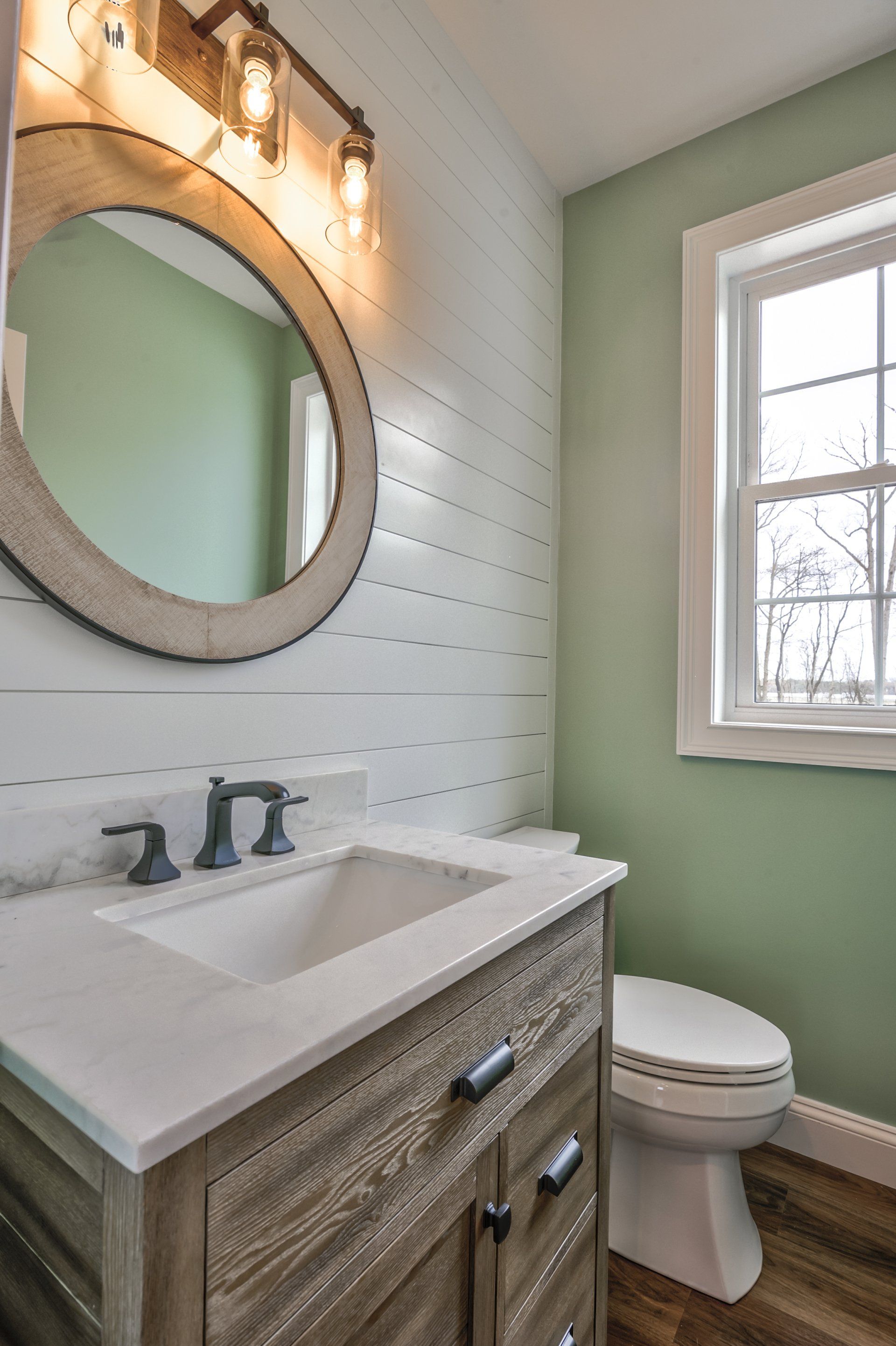 A bathroom with a sink , toilet , mirror and window.