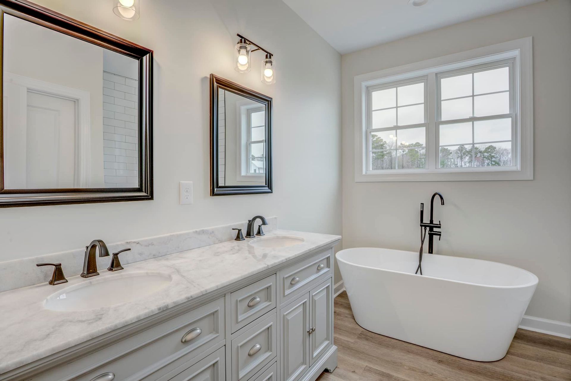 A bathroom with two sinks , two mirrors and a bathtub.