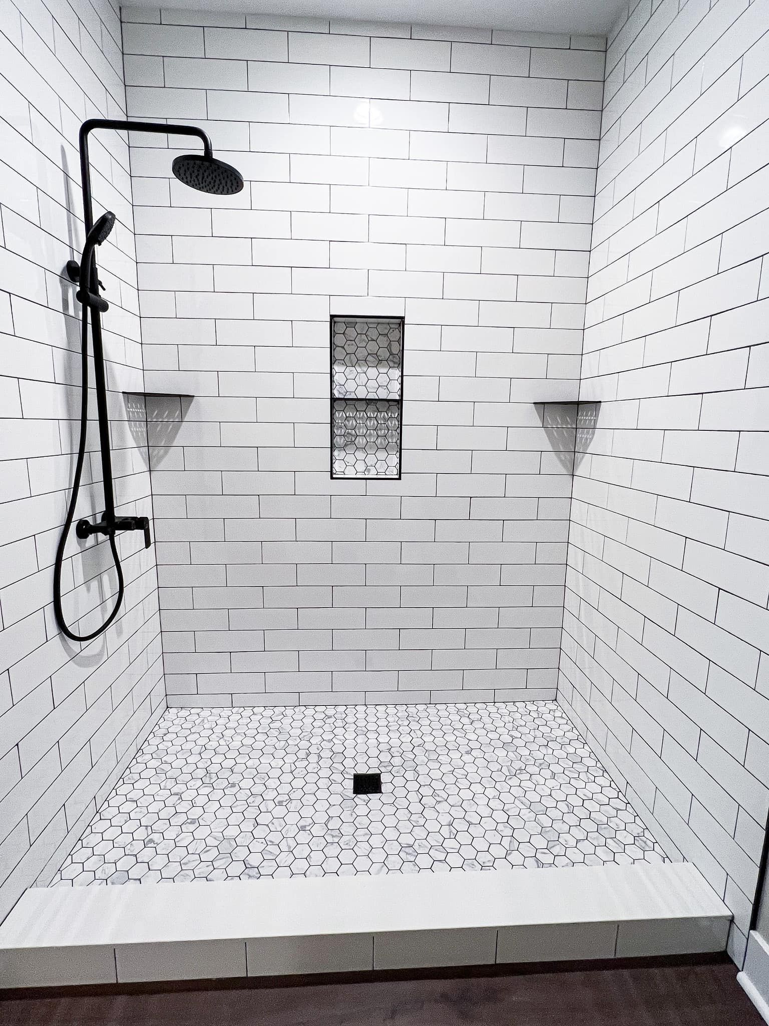 A bathroom with white tiles and a black shower head.