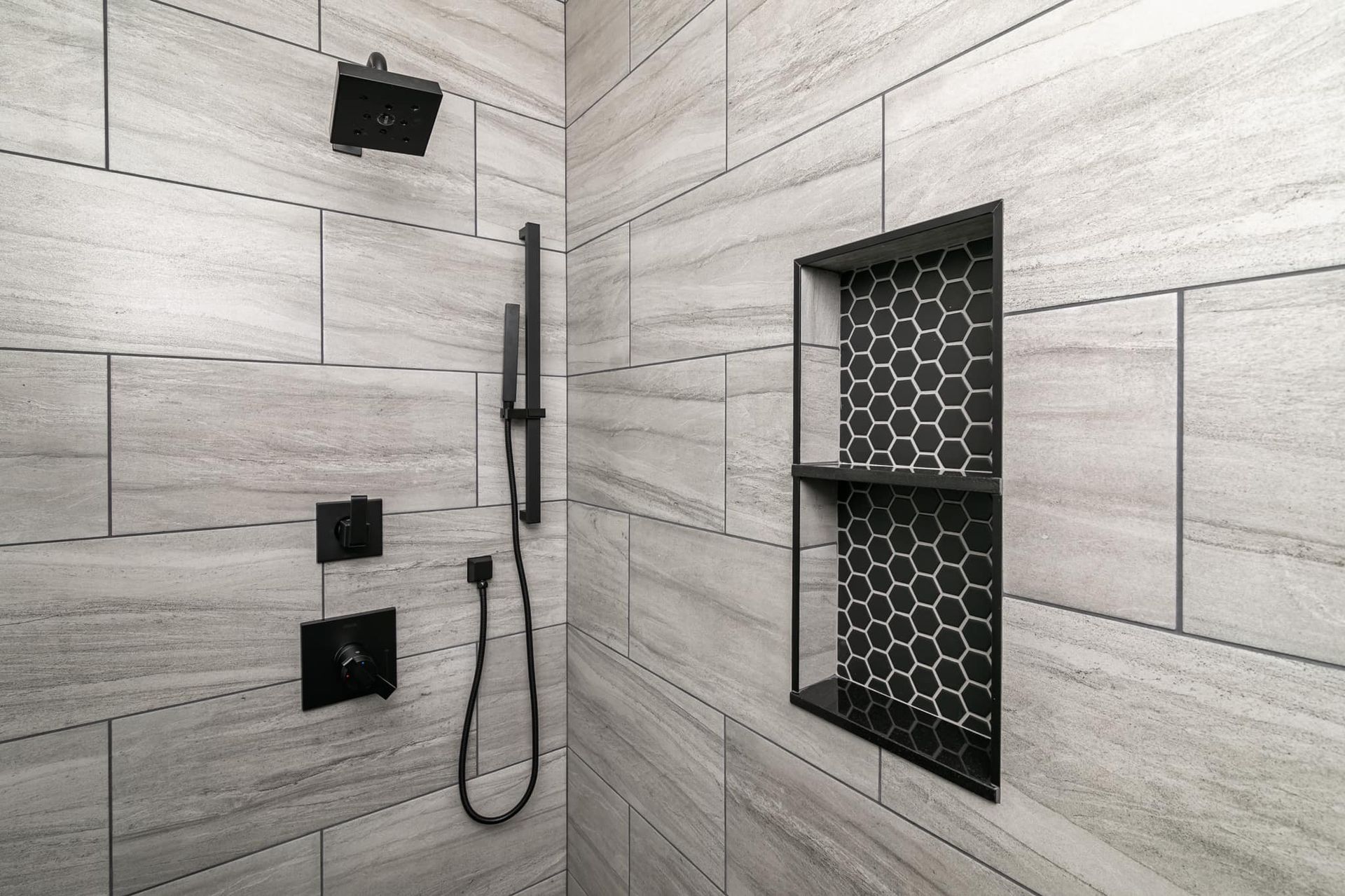A shower with a black shower head and a black shelf.