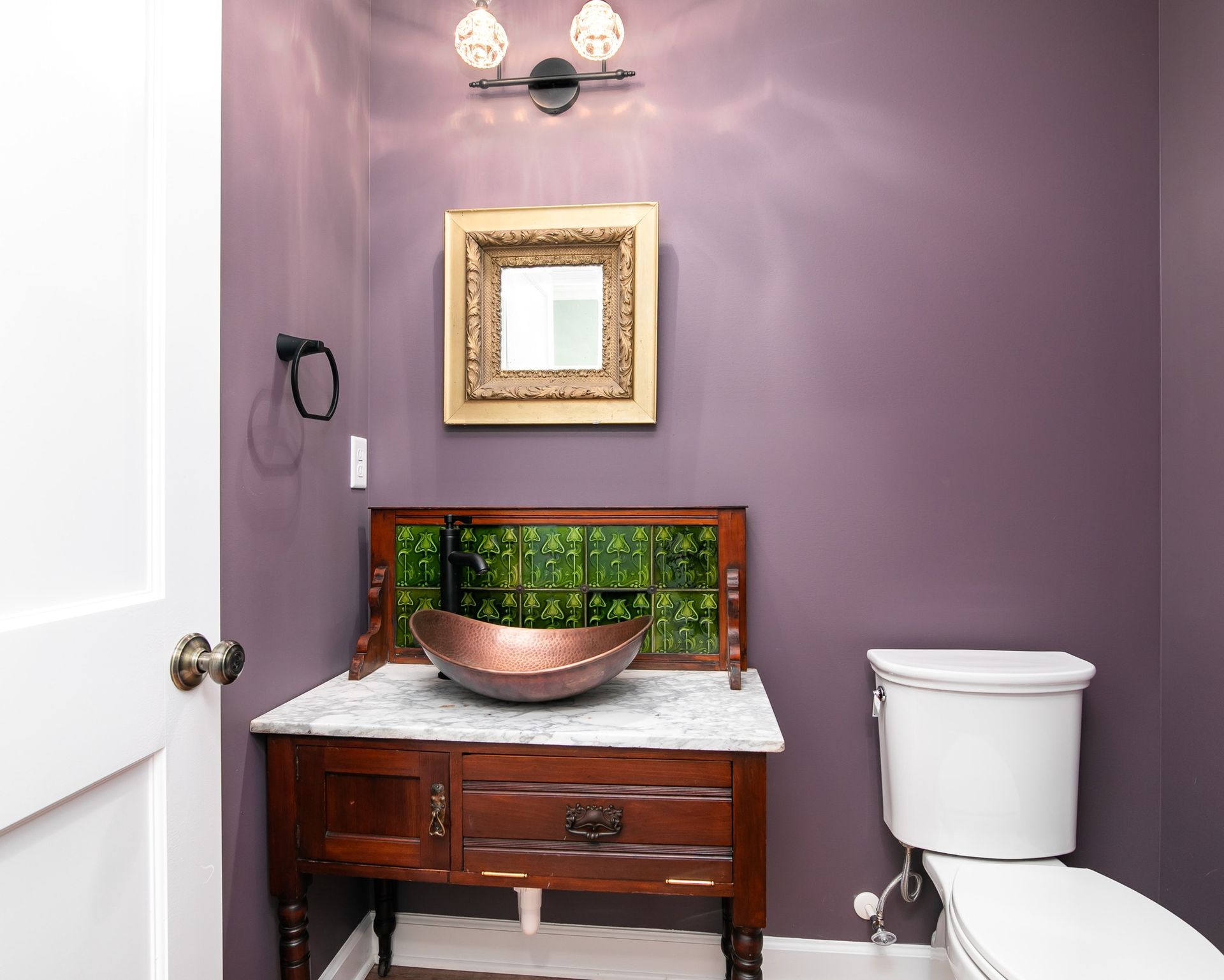 A bathroom with purple walls , a sink , toilet and mirror.