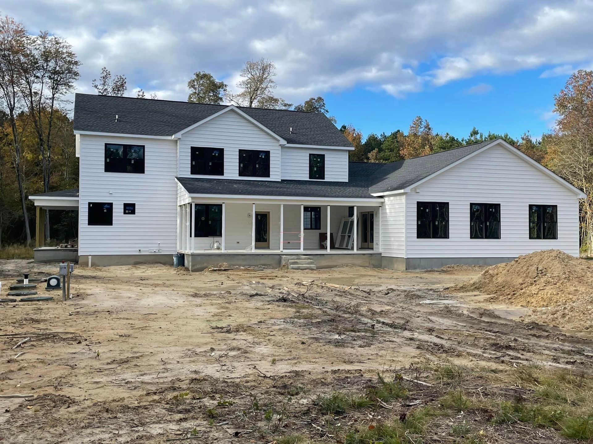 A large white house with a porch is being built in a dirt field.