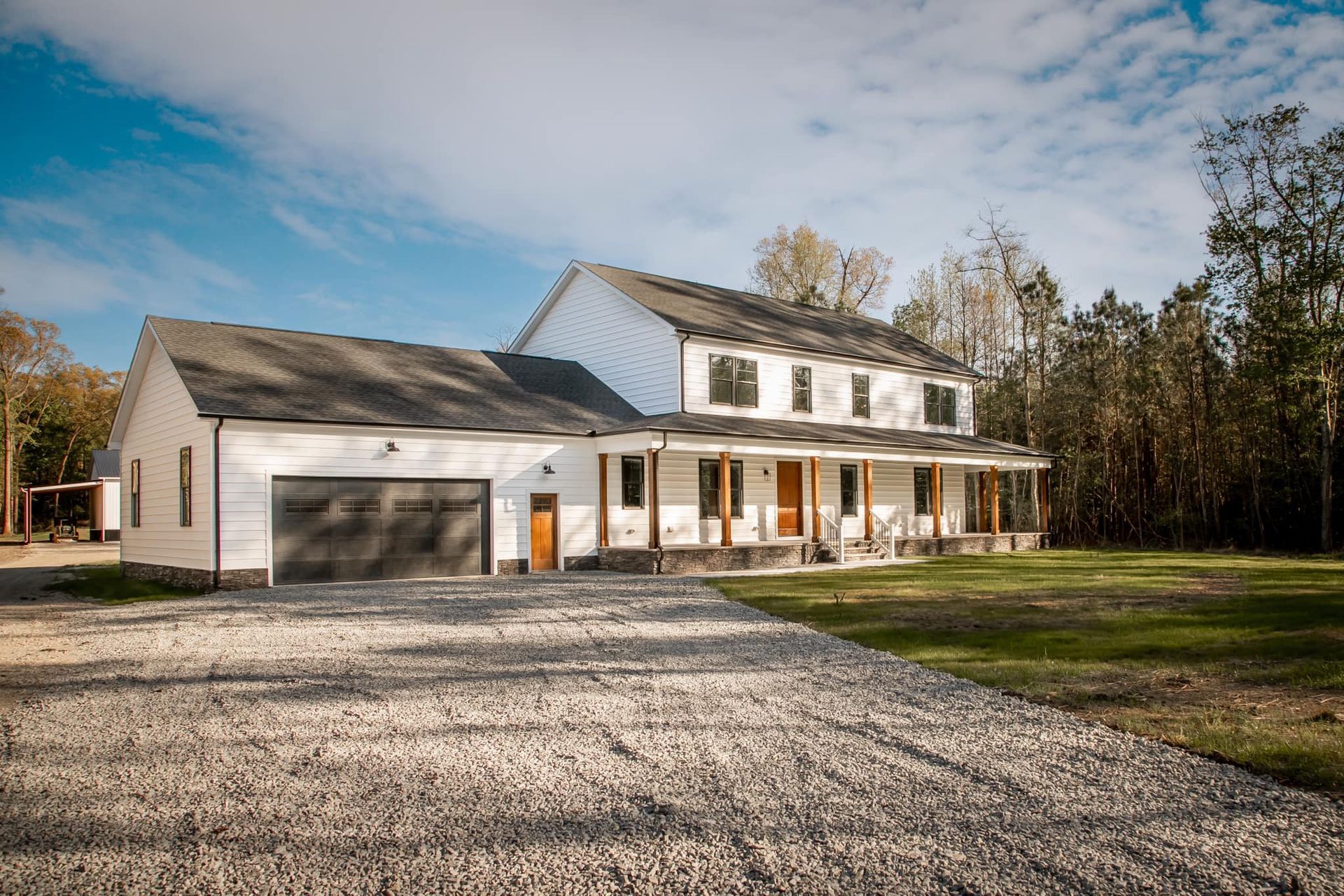 A large white house with a garage and porch is sitting on top of a gravel driveway.