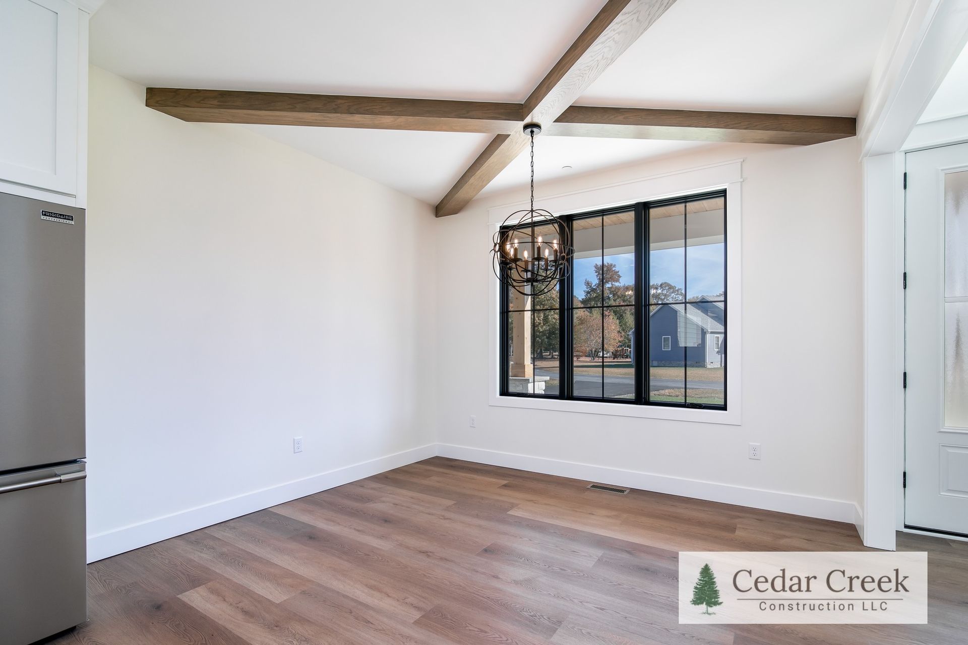 An empty room with hardwood floors, a refrigerator, and a window