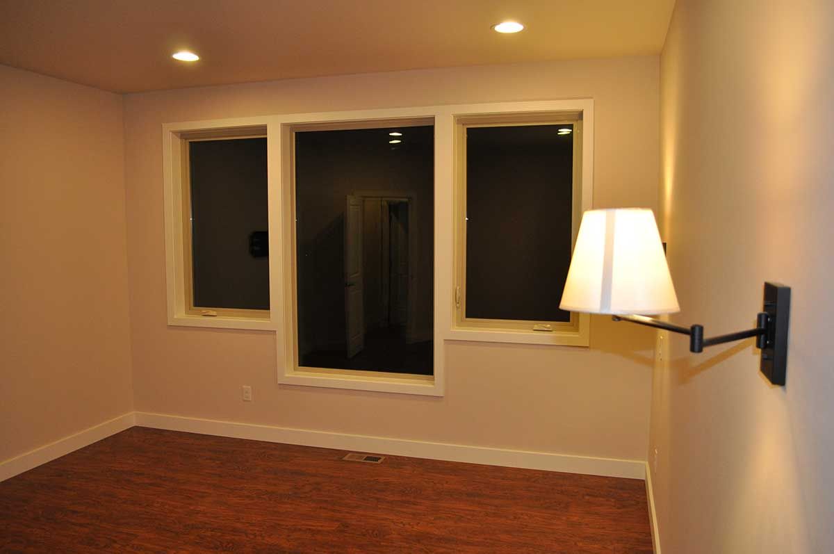 An empty room with three windows and a lamp on the wall