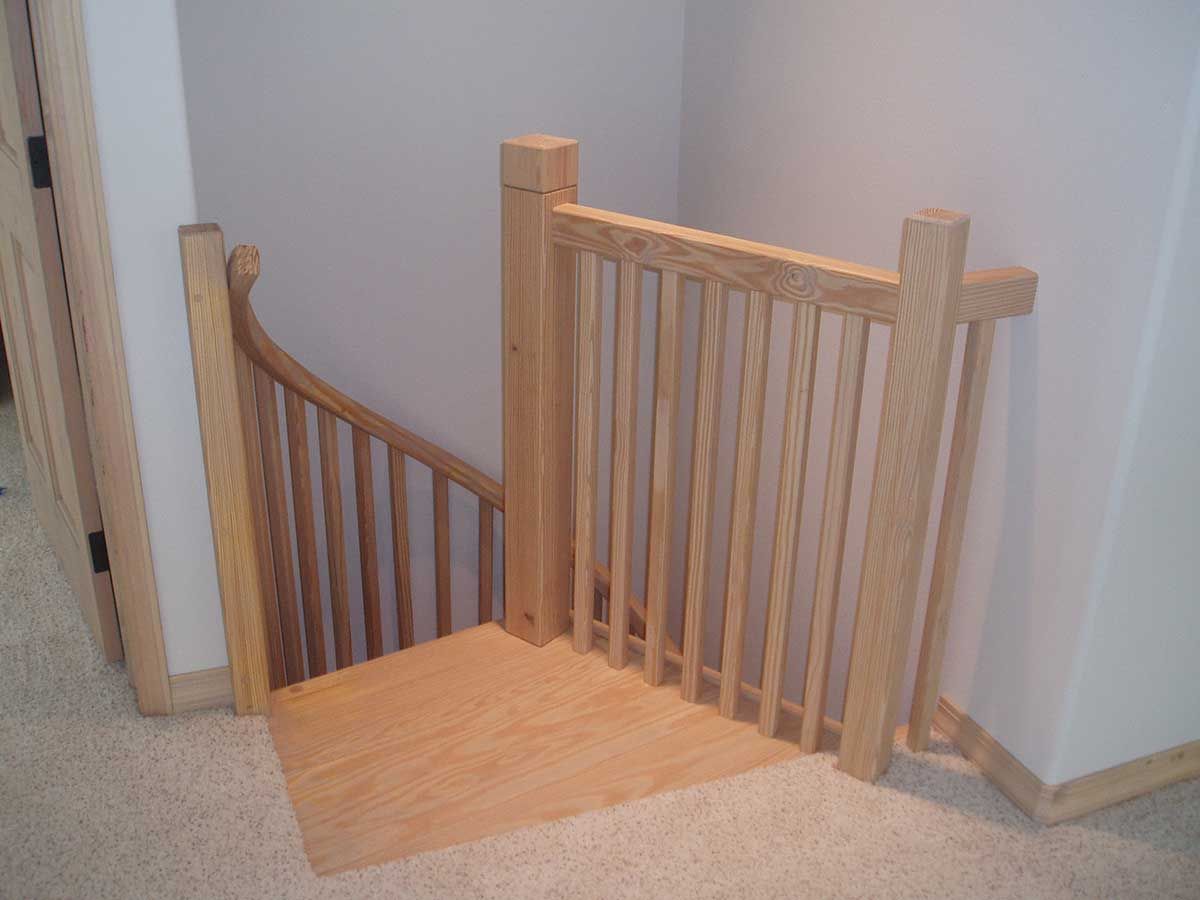 A wooden staircase with a wooden railing in a corner of a room.