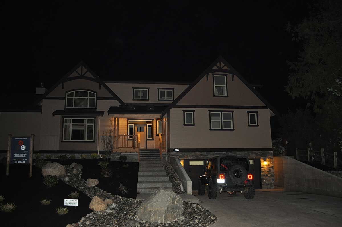 A large house is lit up at night with a jeep parked in front of it.