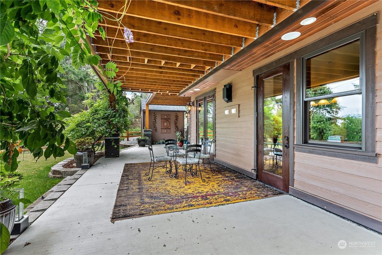 A patio with a table and chairs under a wooden roof.