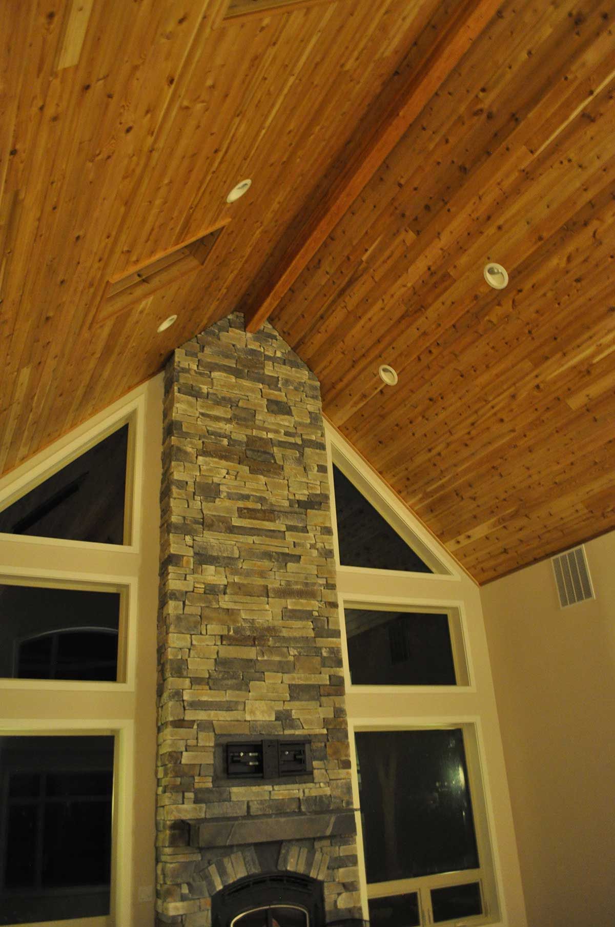 A living room with a stone fireplace and wooden ceiling.
