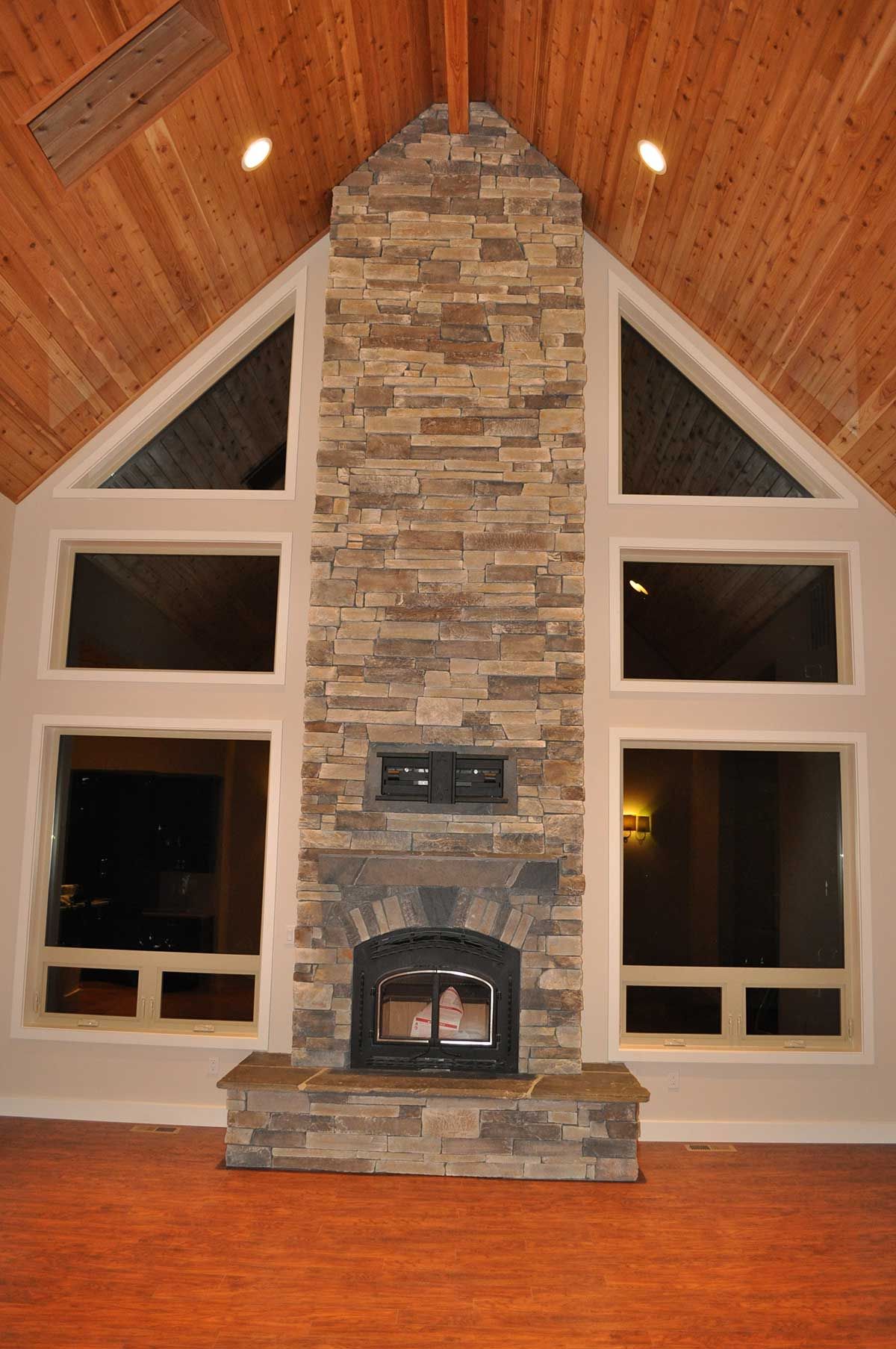 A large stone fireplace in a living room with lots of windows.