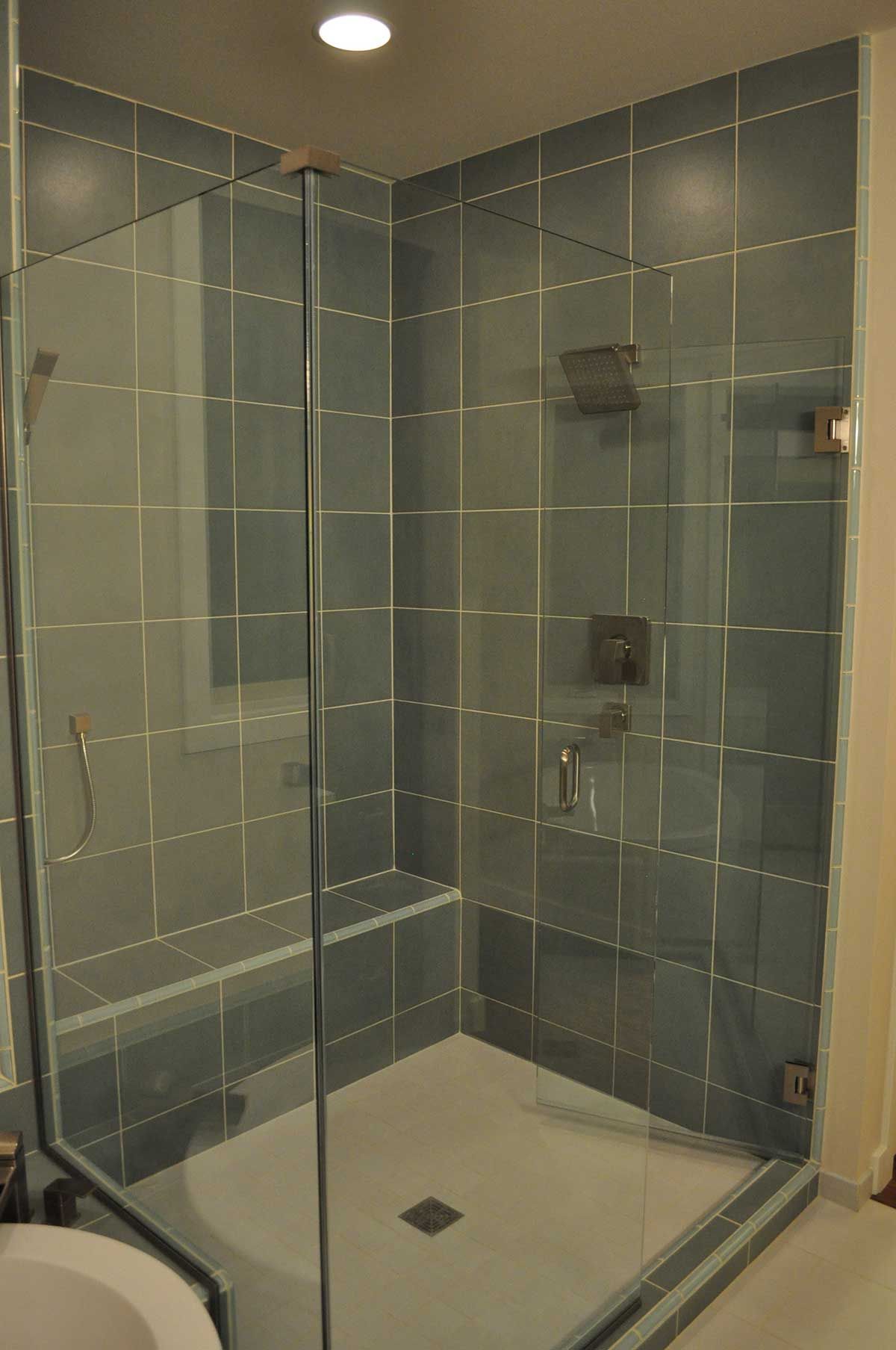 A bathroom with blue tiles and a walk in shower with a glass door.