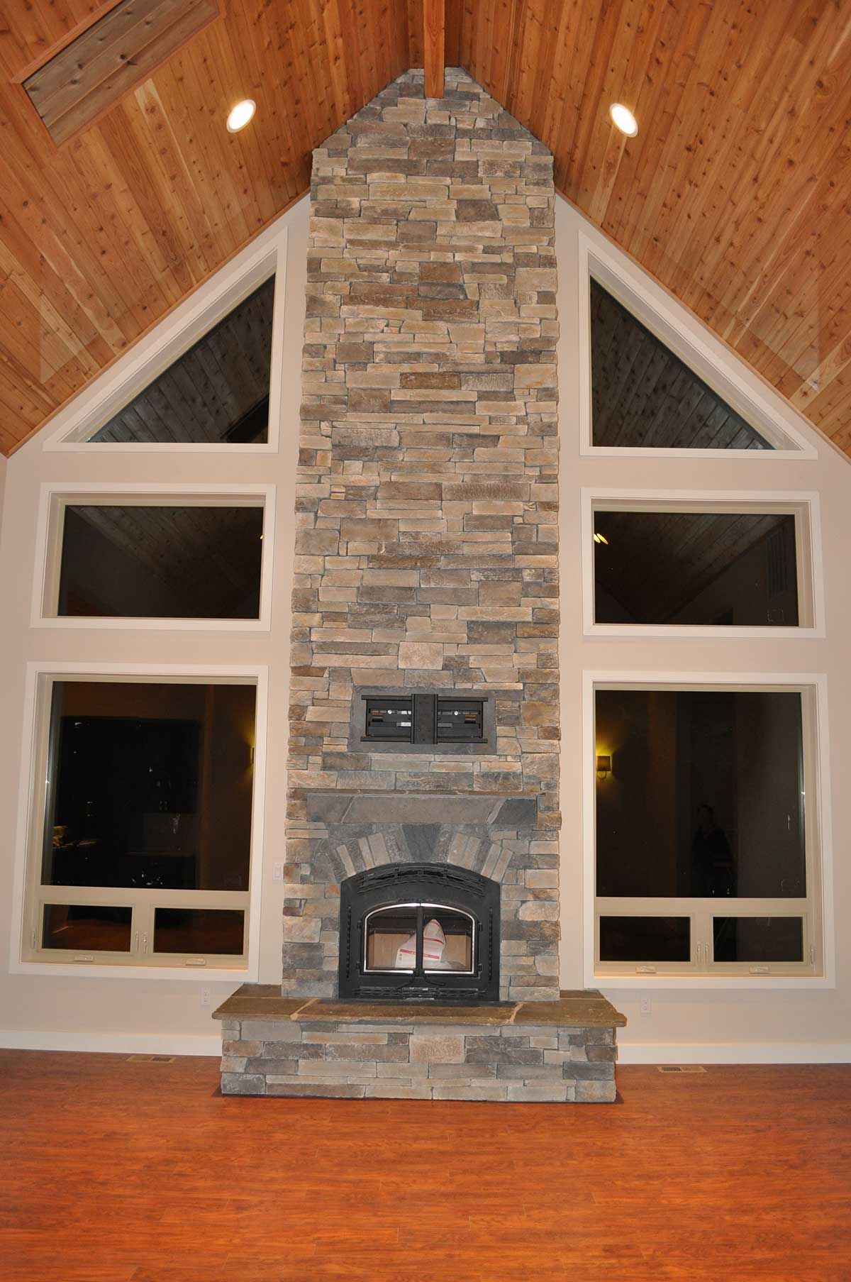 A large stone fireplace in a living room with lots of windows.