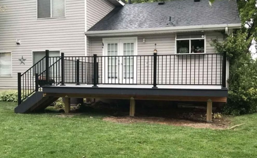 A light gray house with a new, elevated dark gray composite deck featuring black railings and stairs leading to the lawn.