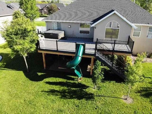 A residential back deck featuring a hot tub, a green spiral slide, and stairs leading down to a green lawn.