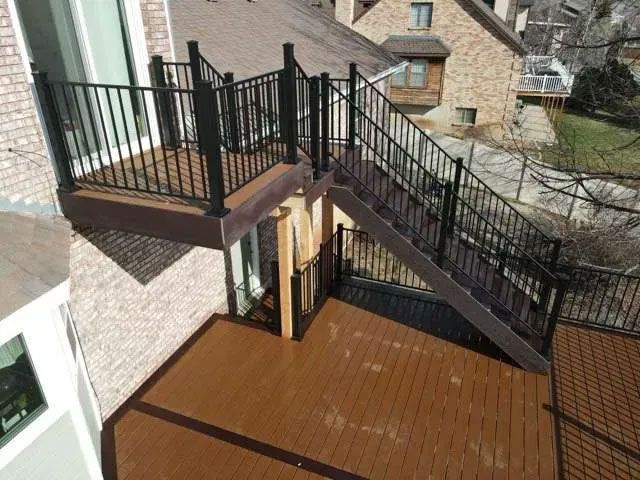 A multi-level outdoor deck made of brown composite wood with black railings and a staircase connecting the two levels.