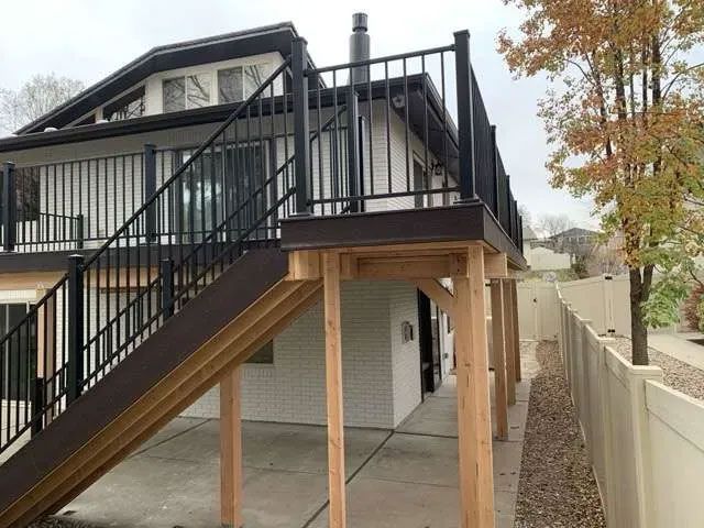 A raised outdoor wooden deck with black railings and a matching staircase leading down to a concrete patio area.