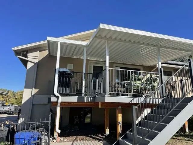 A house exterior featuring a raised wooden deck with a white metal patio cover, black metal railings, and outdoor stairs.