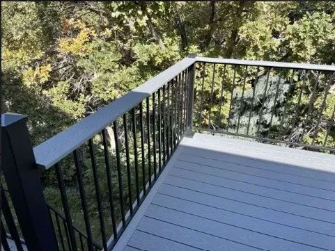 A gray composite deck with black metal railings overlooking a wooded area.
