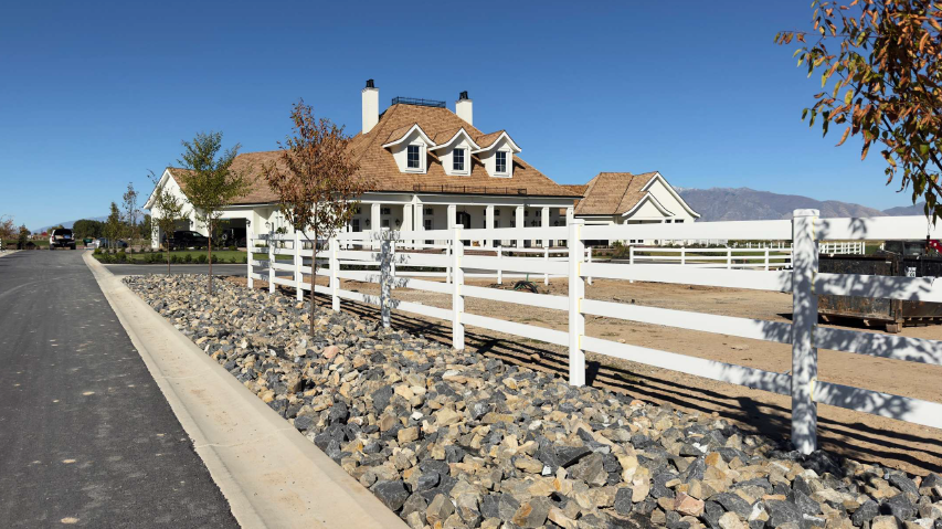 White ranch house with orange roof beside a white fence and road under a clear blue sky