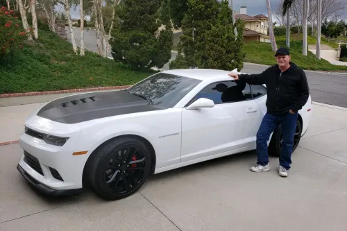 Man leaning on a white sports car parked on a suburban street