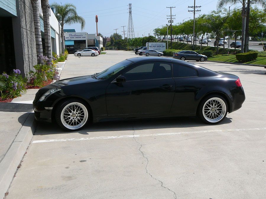 Black coupe parked beside a building on a sunny street.