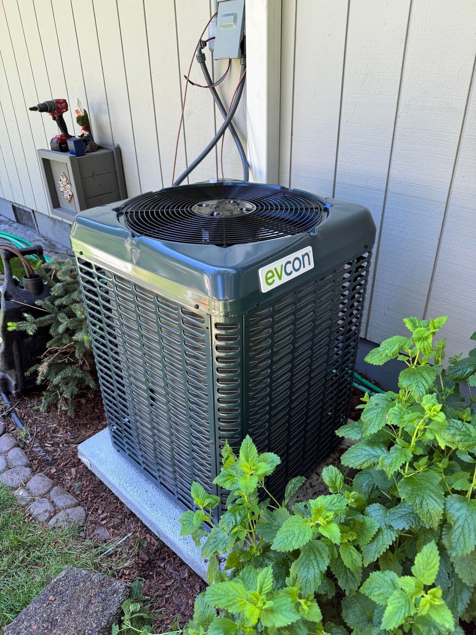 An Evcon air conditioning unit sits outside a white building, surrounded by greenery.