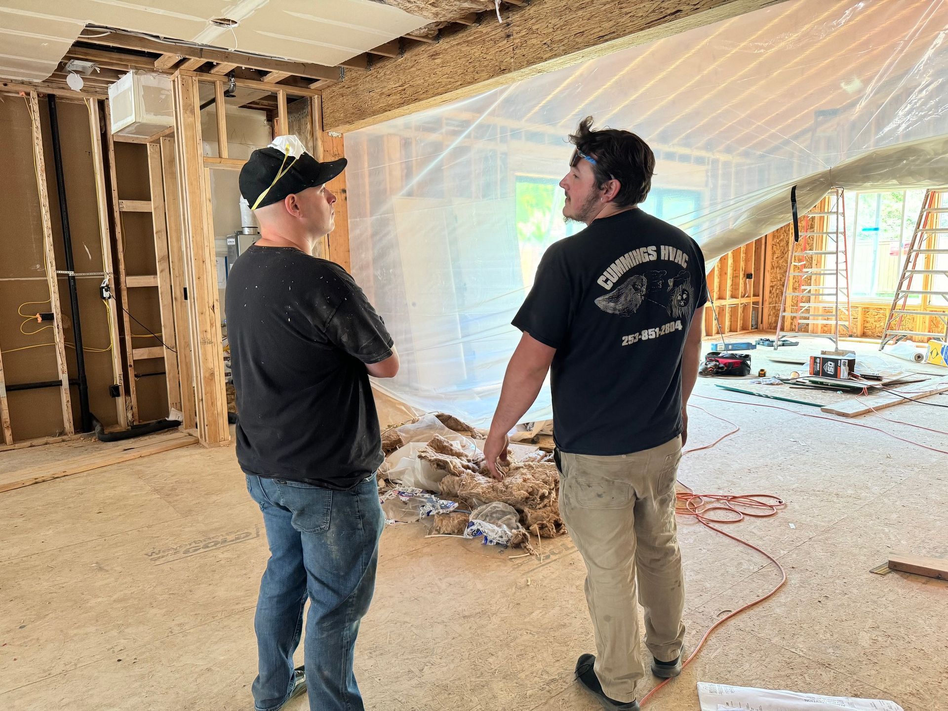 Two men in a room under construction, discussing; exposed walls, plastic sheeting, debris.