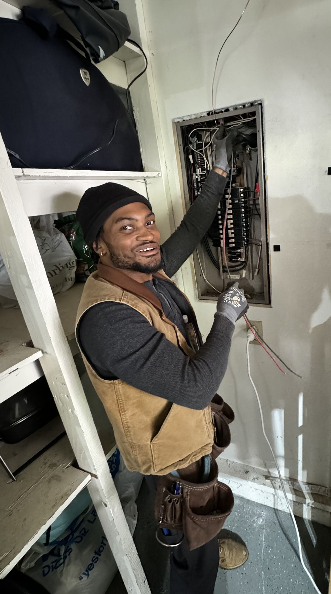 Electrician working on a circuit breaker panel, wearing a tool belt and gloves.