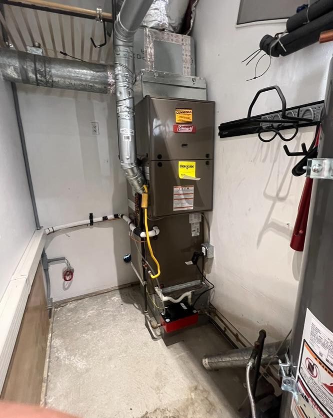 Furnace and water heater in a utility closet with ductwork and piping. Gray, white, and red components.