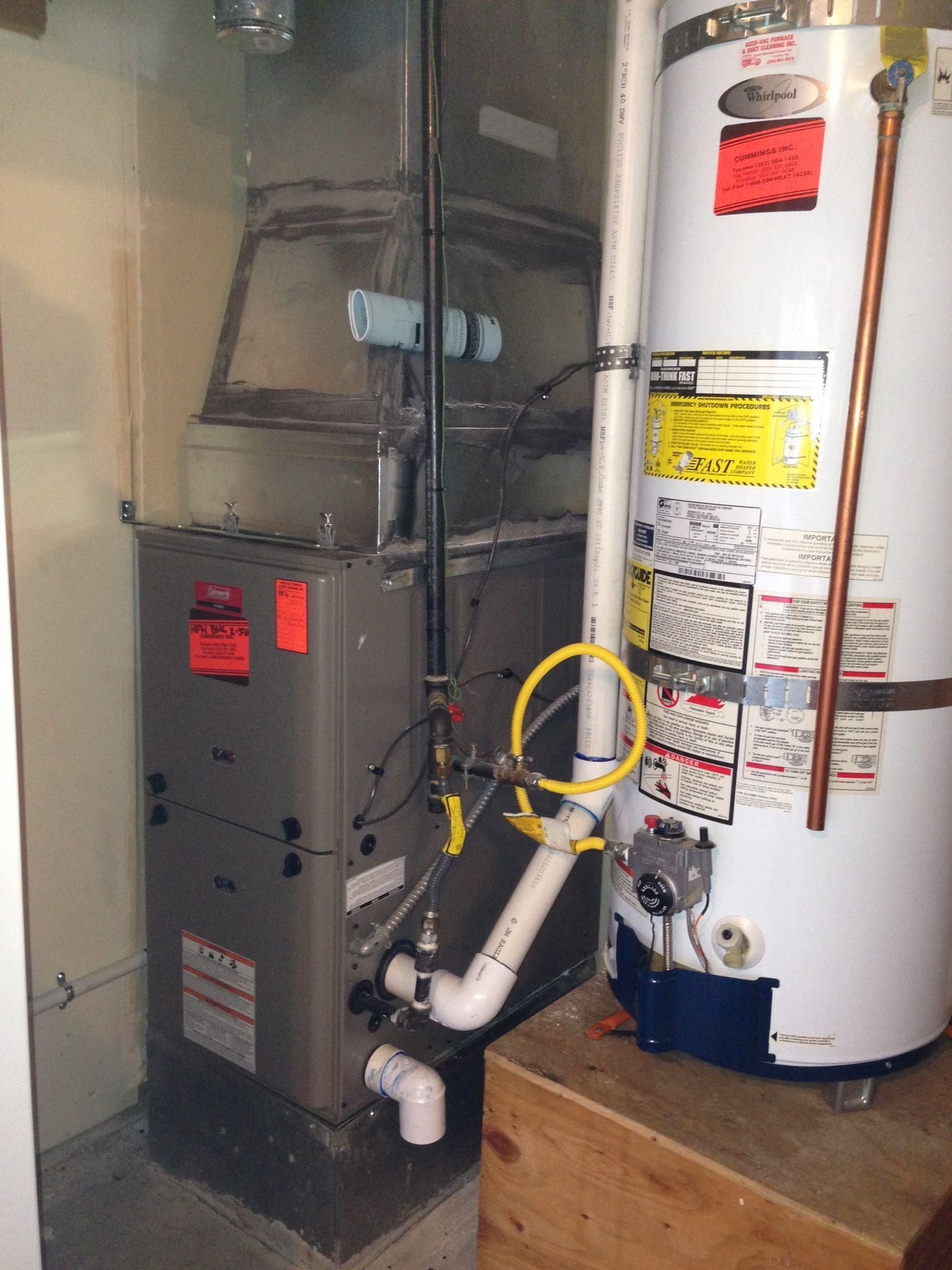 Furnace and water heater in a utility room. Gray metal units with various pipes and labels.