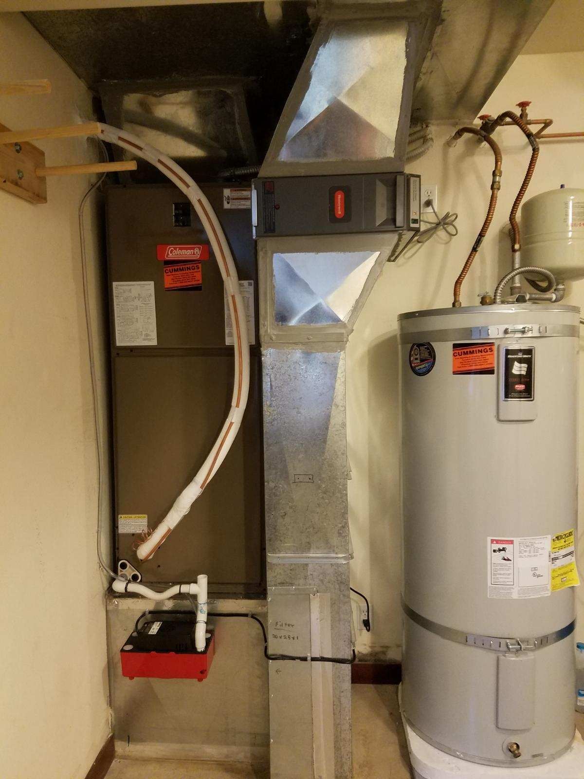 Furnace and water heater in a utility room. Metal ductwork and copper pipes are visible.